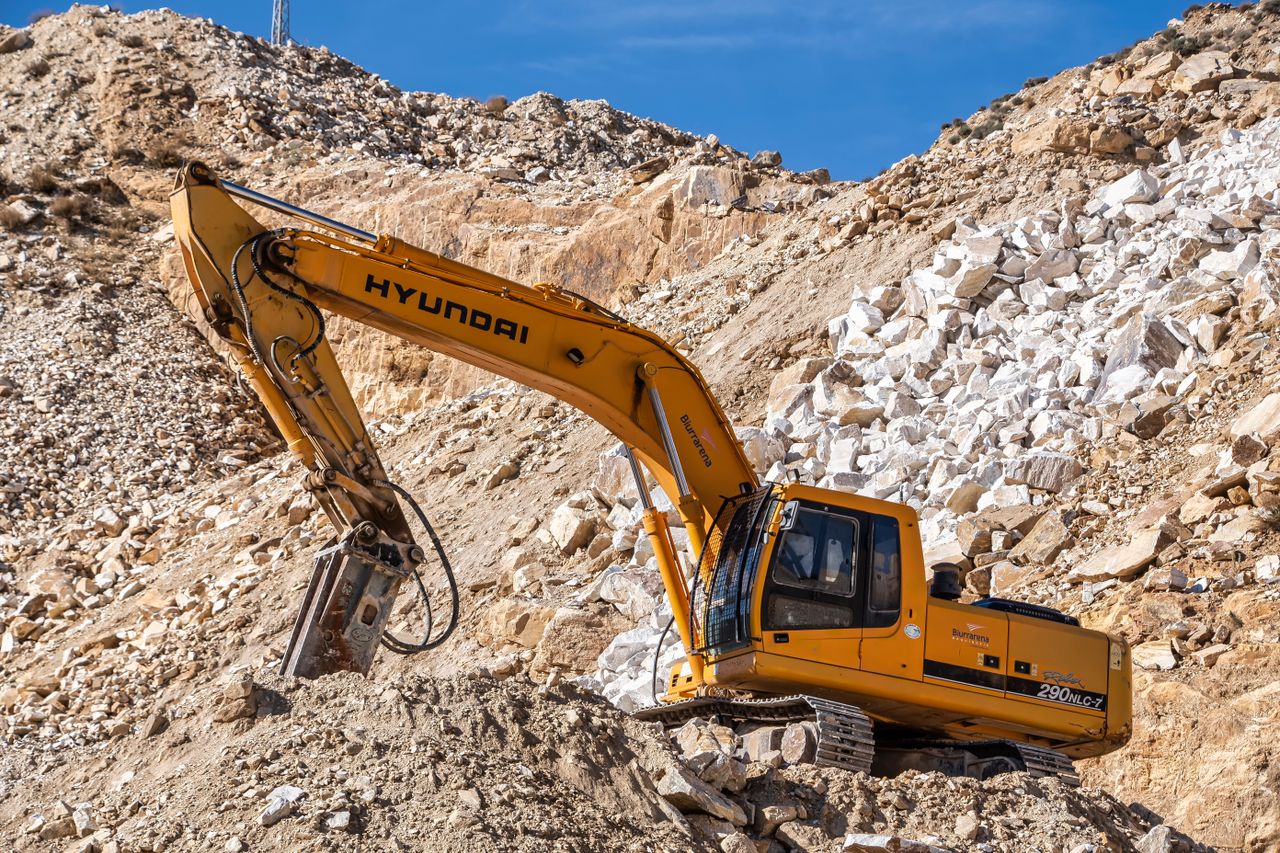 Services Yellow Hyundai excavator operating in a rocky quarry under a clear blue sky. Perfect for industrial themes.